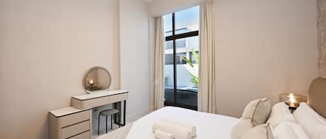 A hotel room with a bed, a desk, a chair, a mirror, and a view of the outside.