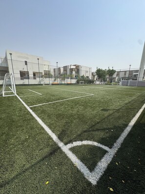 Un campo deportivo con porterías y bancos, rodeado por una valla y edificios.