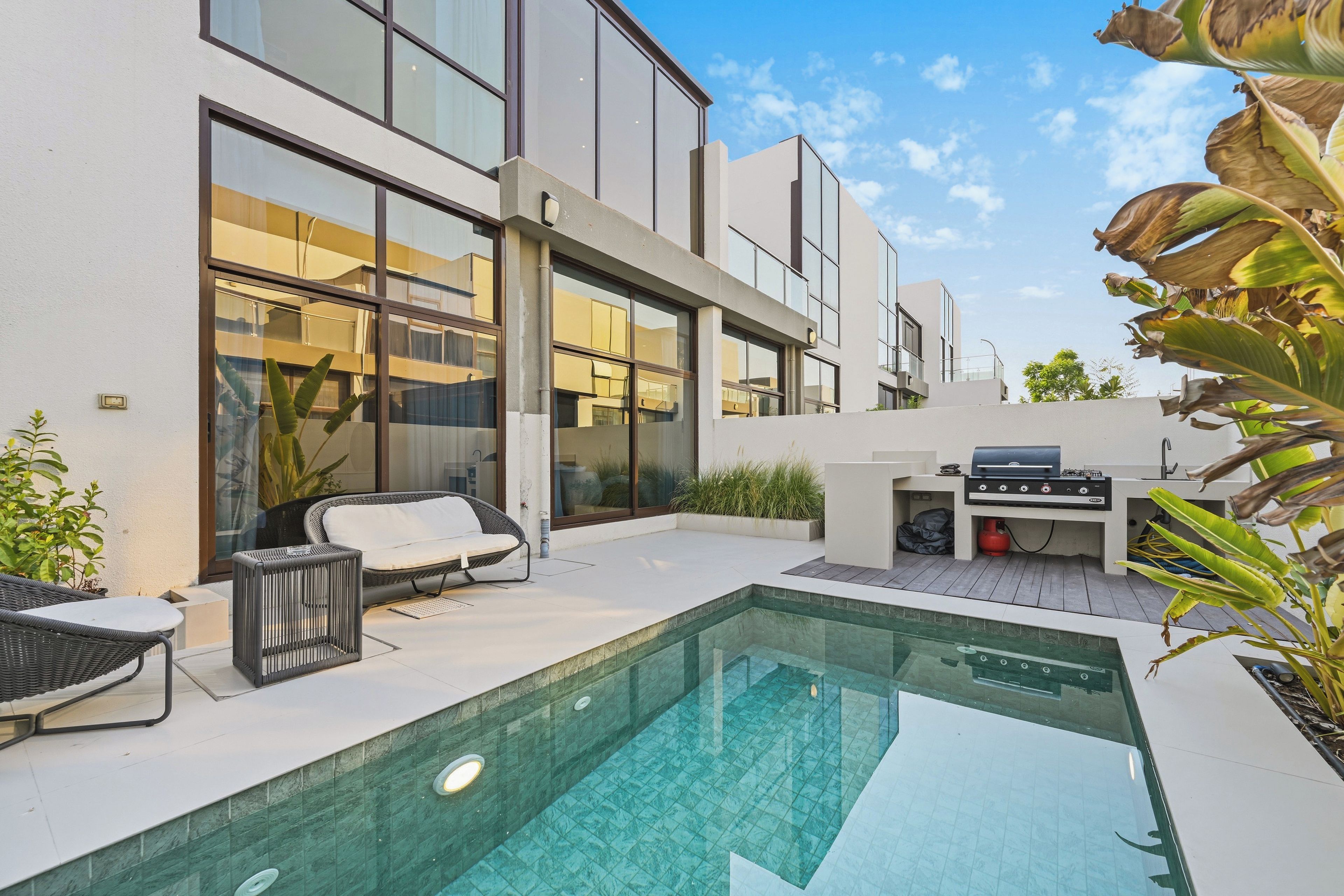 Un espace piscine extérieur moderne, doté d’un barbecue intégré et de coins salon.