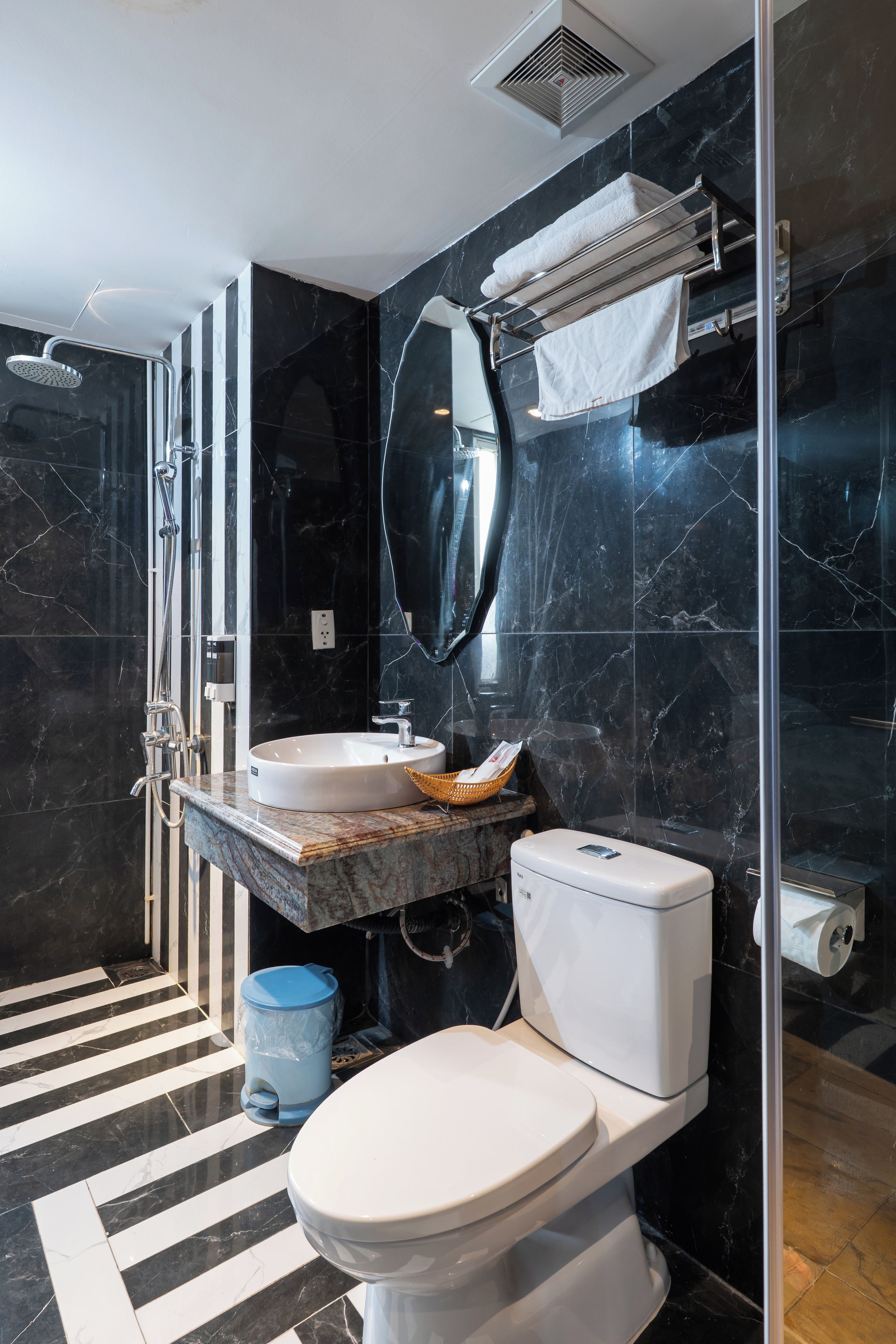 A modern bathroom with a black marble sink, a white toilet, and a glass-enclosed shower.
