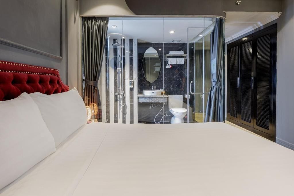 Une chambre moderne avec un grand lit, une salle de bain fermée par des parois de verre et une tête de lit rouge.