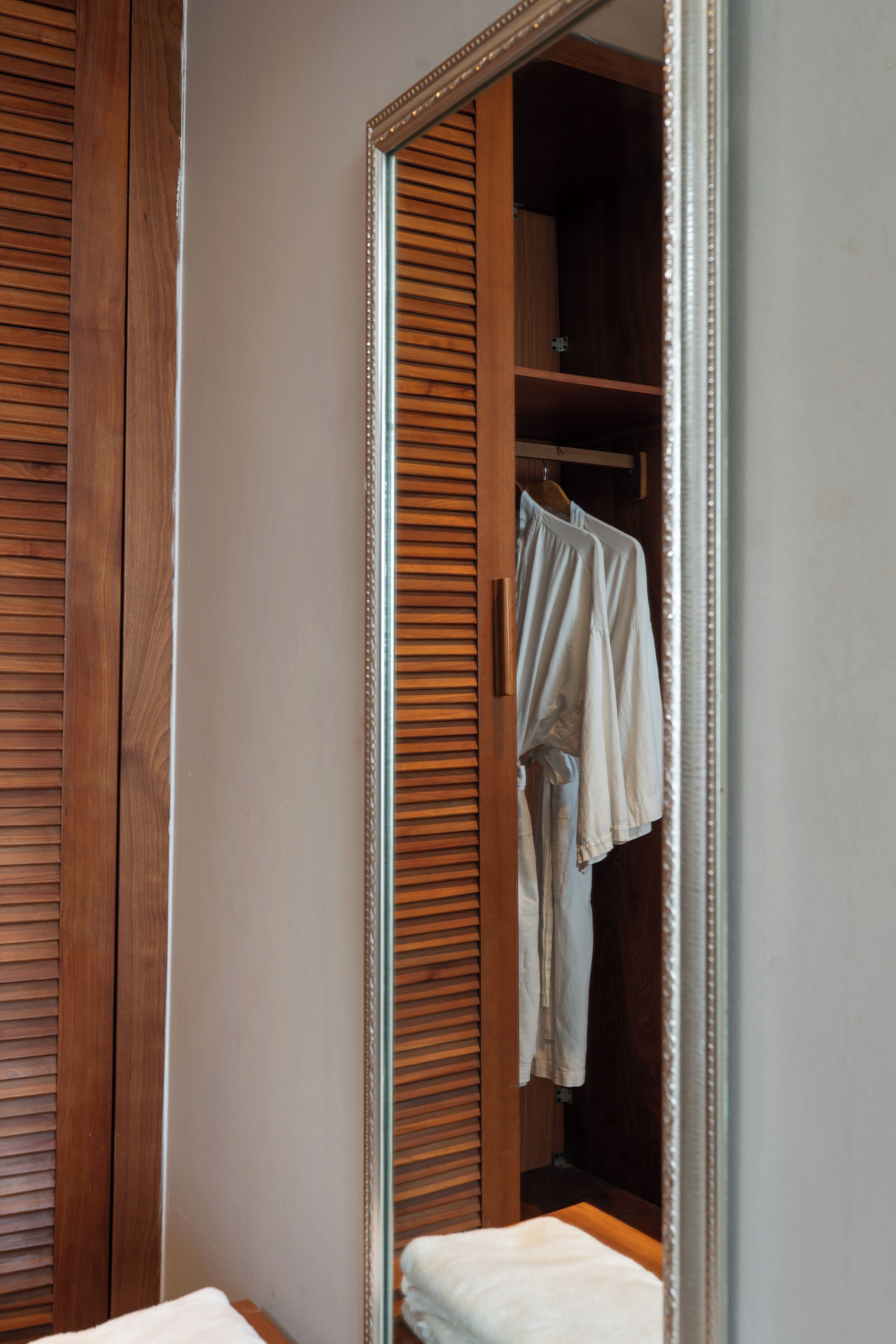 A wooden wardrobe with a mirror reflecting a hanging garment.
