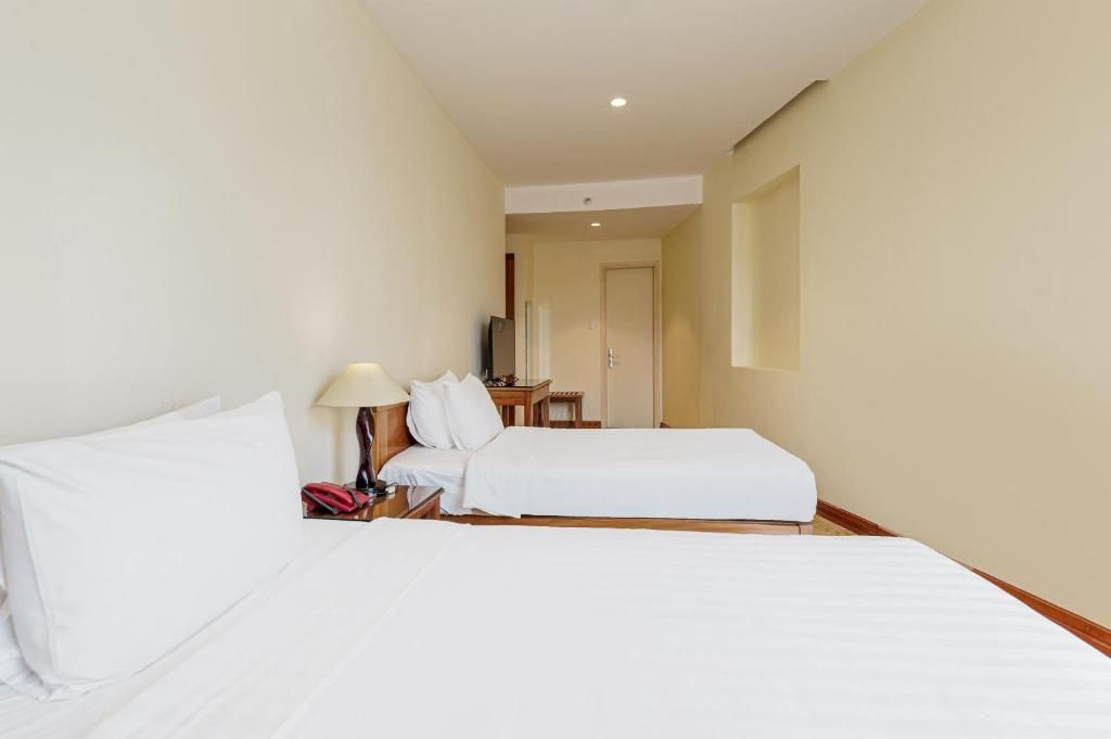Une chambre d’hôtel avec deux lits, une table de chevet avec une lampe et une petite table avec une chaise.