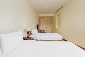 Quarto de hotel com duas camas, uma mesa de cabeceira com abajur e uma pequena mesa com uma cadeira.