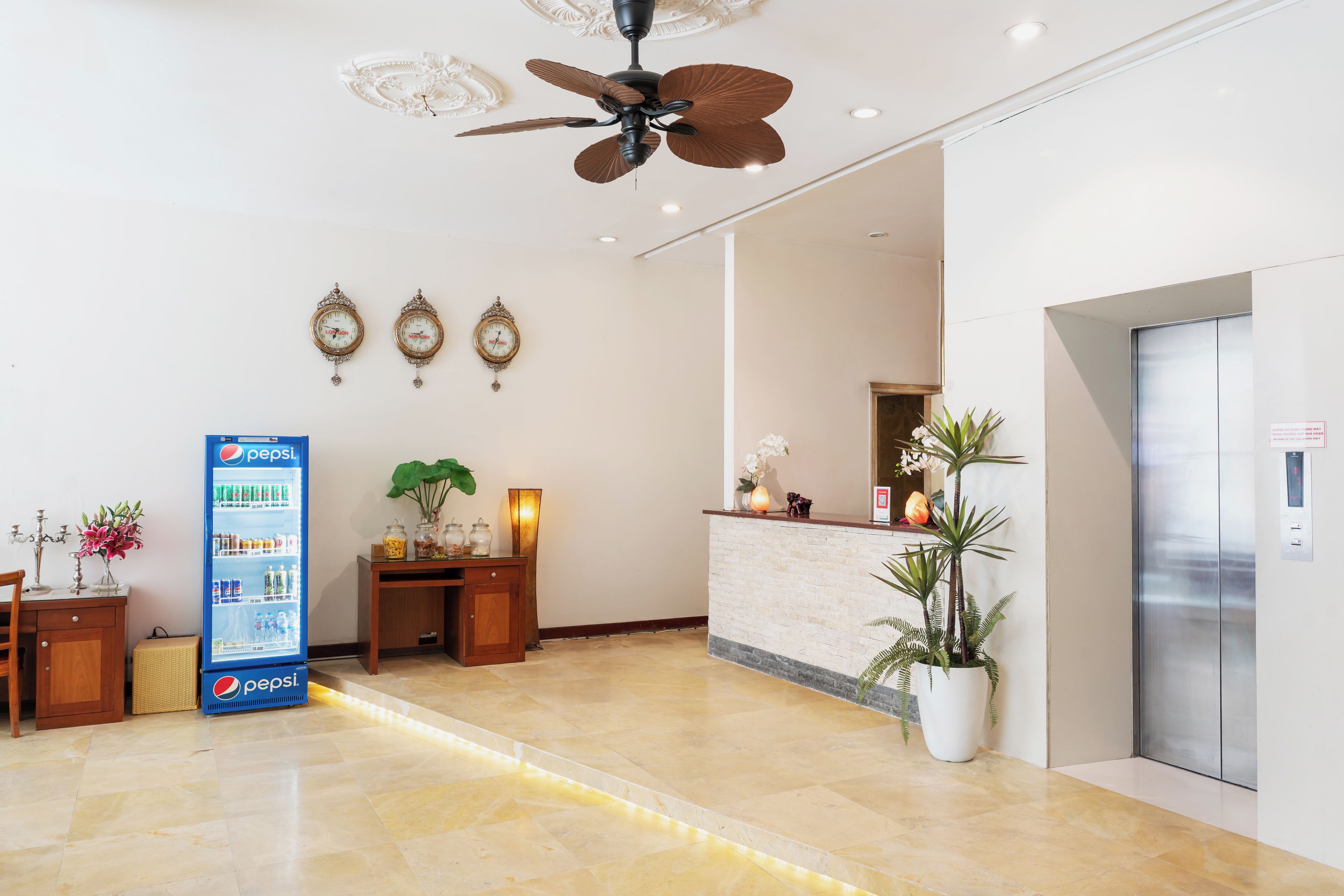 Een hotellobby met een receptiebalie, een klok, een plafondventilator en een automaat.