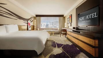 A hotel room with a bed, a desk, a television, and a view of the city.