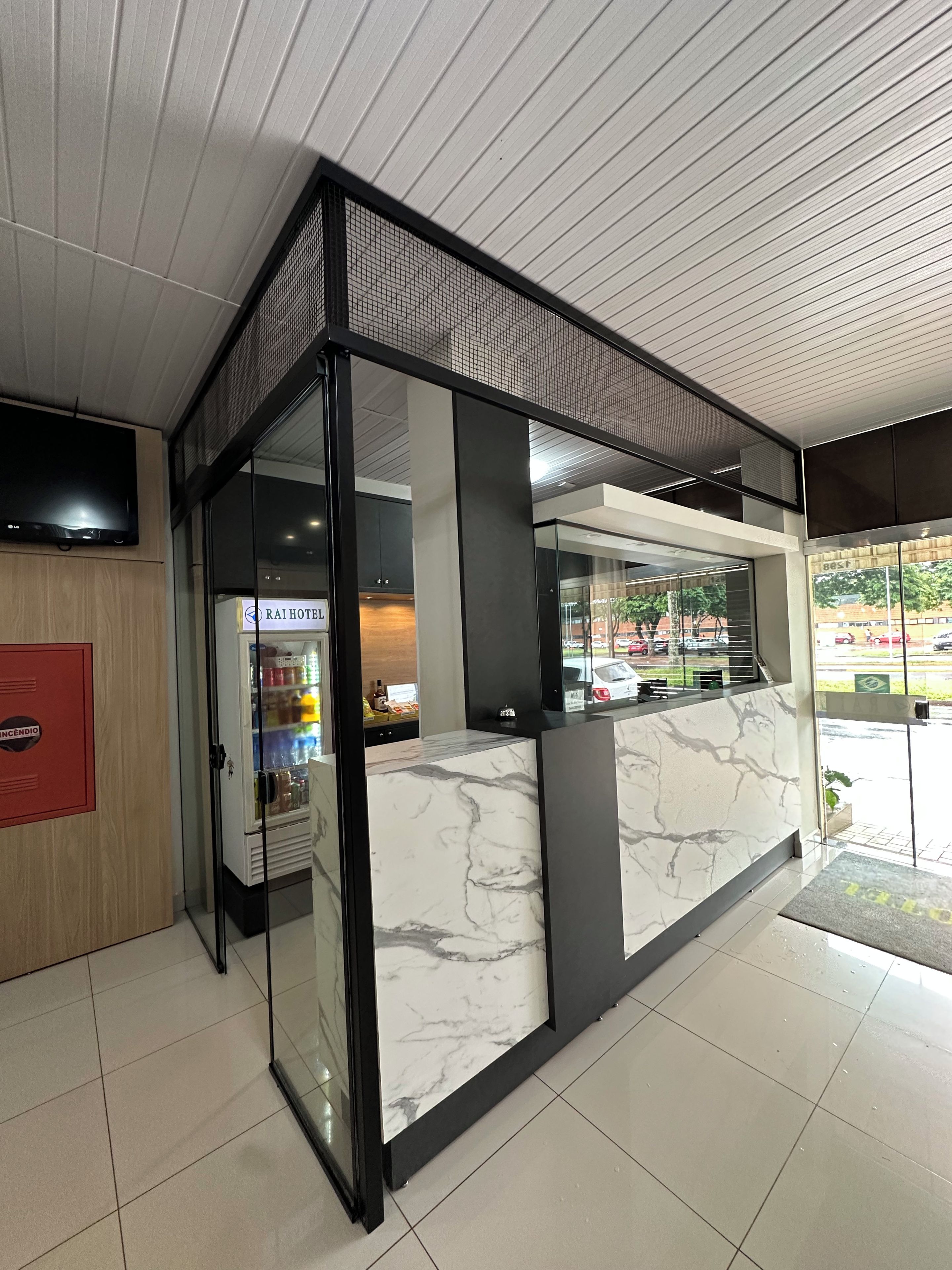 A hotel reception area with a marble counter, glass doors, and a flat-screen TV mounted on the wall.