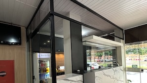 Zona de recepción de hotel con mostrador de mármol, un televisor montado en la pared y una puerta de cristal que da al interior.