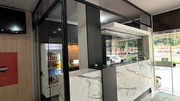 A hotel reception area with a marble counter, glass doors, and a flat-screen TV mounted on the wall.
