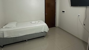 Una habitación con una cama, una puerta, un televisor de pared y una lámpara en el techo.