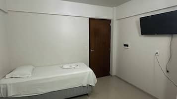 A room with a bed, a door, a wall-mounted TV, and a ceiling light.