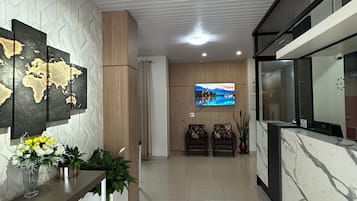 A reception area with a marble reception desk, a world map artwork, a flat-screen TV, and a plant arrangement.