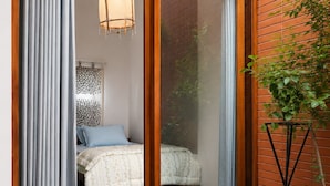 Un dormitorio con puerta corrediza de vidrio, una cama con colcha estampada, una lámpara colgante y una planta en maceta.