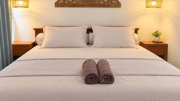 Una cama bien tendida con dos toallas enrolladas, un adorno en la pared y dos lámparas de noche.