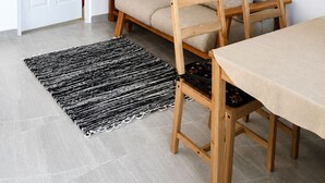 Una habitación con una puerta blanca, un sofá beige, una silla de madera, una mesita pequeña, un alfombra blanco y negro, y un cuadro en la pared.