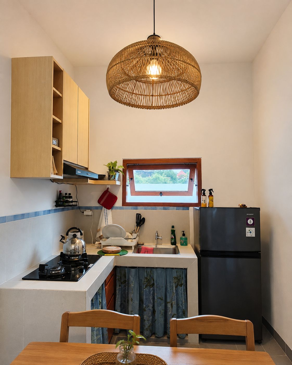 Una cocina compacta con estufa a gas, refrigerador, ventana con vistas y lámpara colgante.