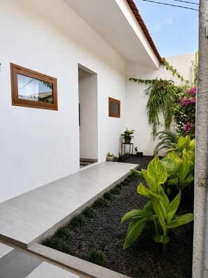 Una casa moderna con diseño depurado, que presenta un camino hacia una puerta, un pequeño jardín con plantas y una pared exterior blanca.