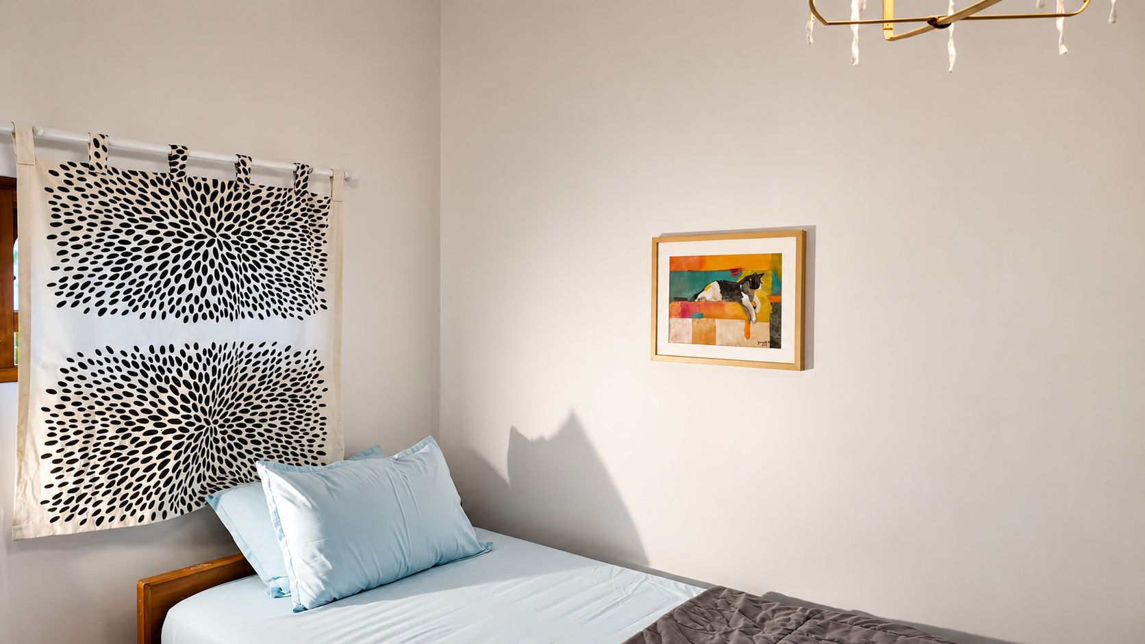 Un dormitorio con una cama, un ventanal con cortina estampada, un cuadro enmarcado en la pared y una araña.