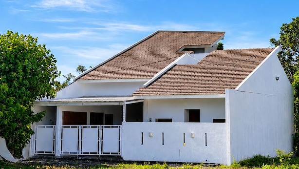 Una casa de un piso con techo inclinado, fachada blanca y balcón.