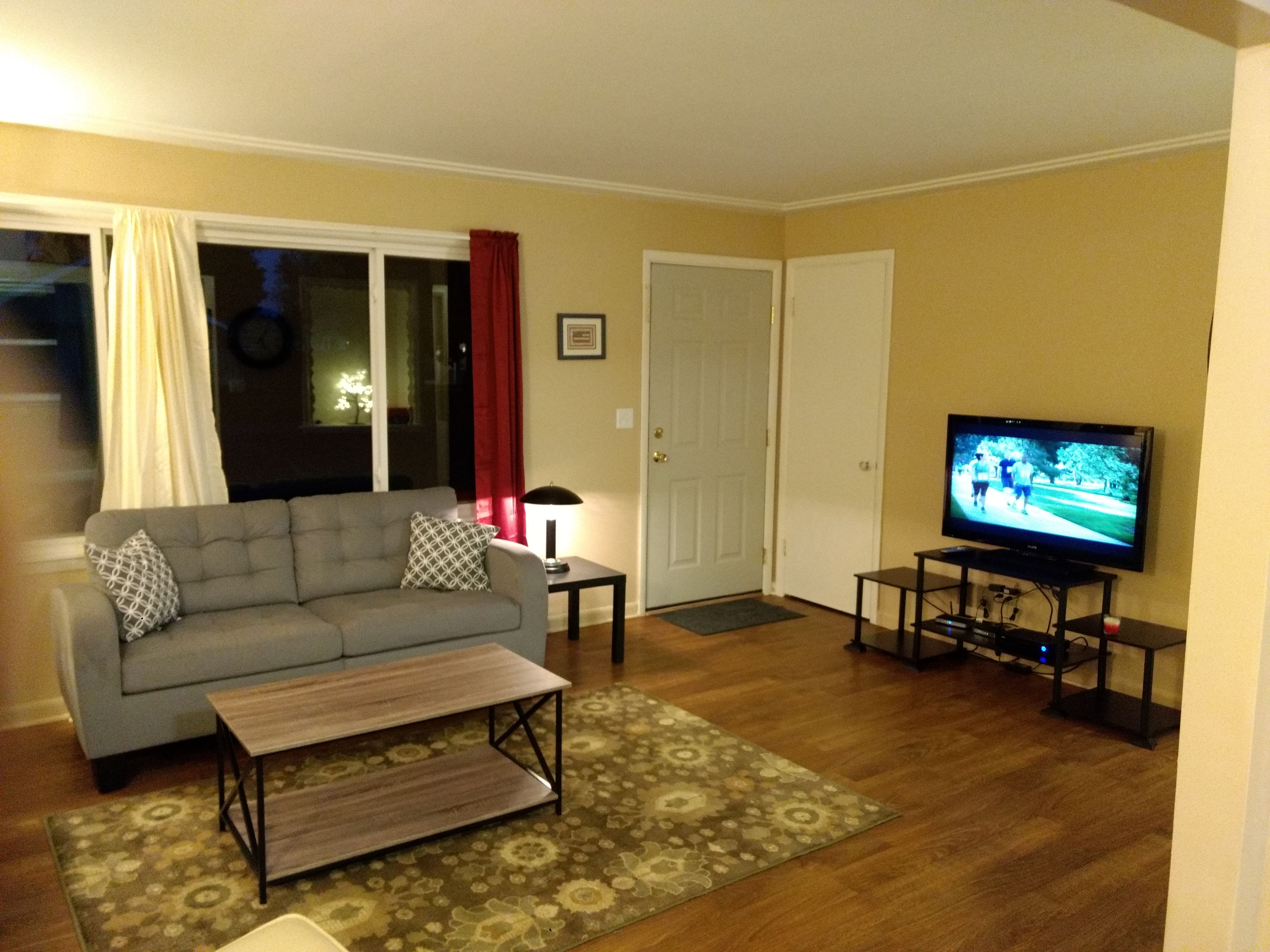 A living room with a sofa, a coffee table, a television, and a door.