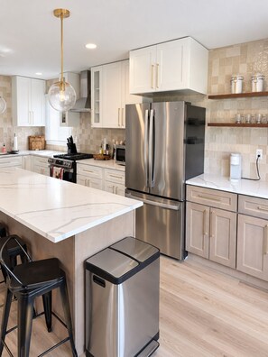 A modern kitchen with a central island, stainless steel appliances, and a hanging light fixture.