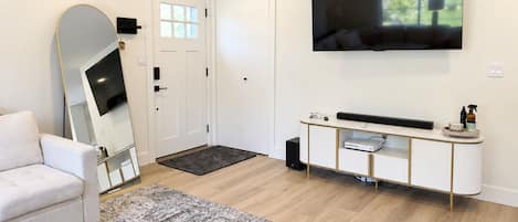 Una sala de estar moderna con un sofá blanco, un espejo grande, un televisor de pantalla plana y un mueble bajo con dispositivos electrónicos.