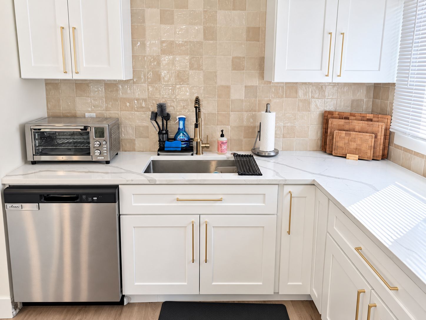 A modern kitchen with white cabinets, a stainless steel dishwasher, a built-in toaster oven, and a sink with a faucet.