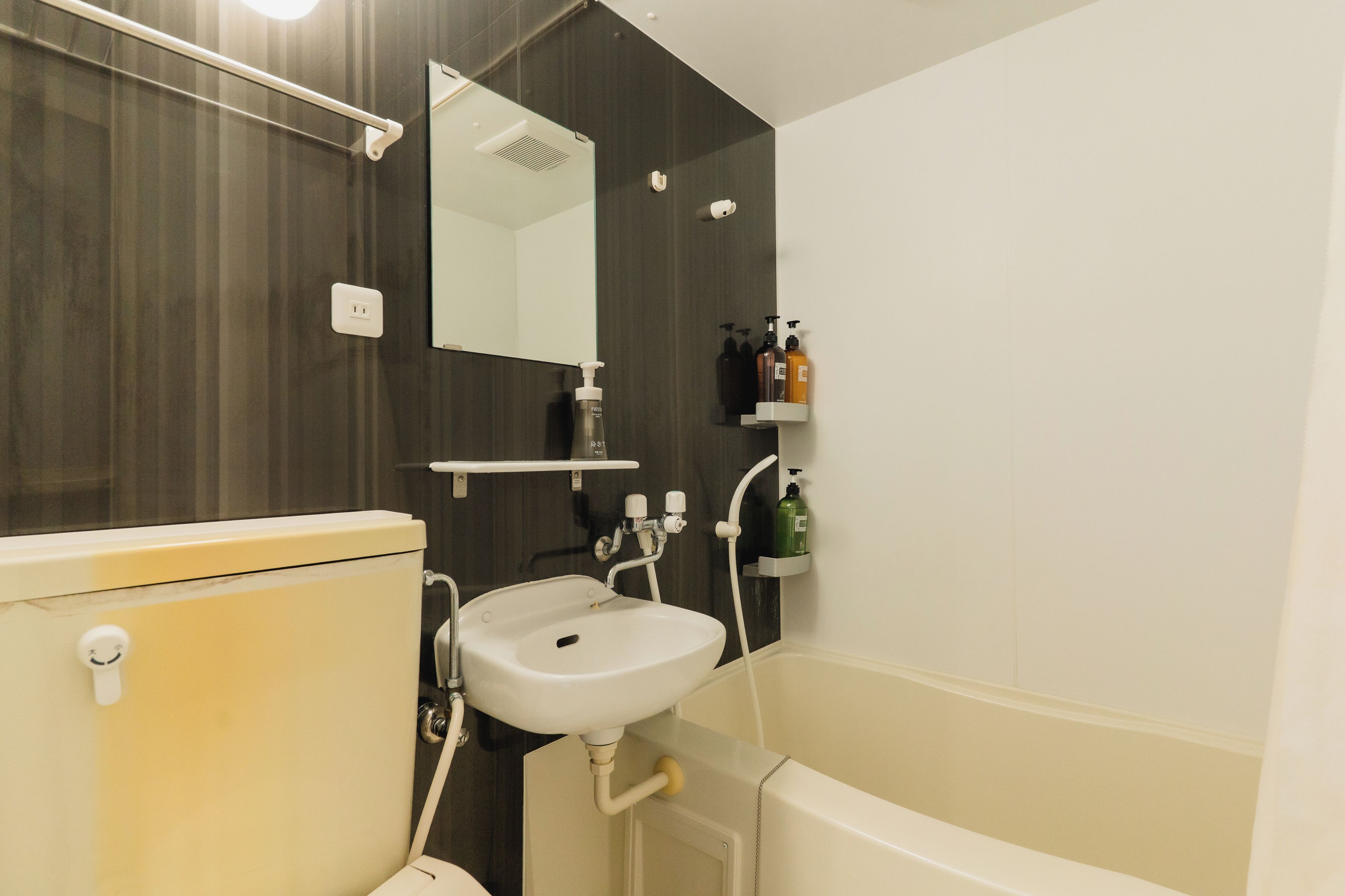 A bathroom with a toilet, sink, and bathtub. There is a mirror above the sink and a shelf with toiletries.