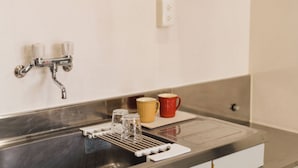 Een keukenzink met een kraan, een koffiezetapparaat en twee mokken op het aanrecht.