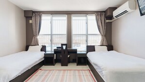 Een hotelkamer met twee enkele bedden, een bureau met een stoel en een groot raam met gordijnen.