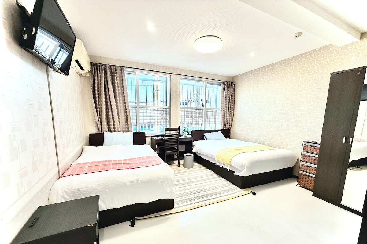 Habitación de hotel con dos camas, un escritorio, una silla, un televisor y una ventana con cortinas.