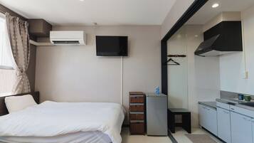 A hotel room with a bed, an air conditioning unit, a television, a small refrigerator, a mirror, and a kitchenette.