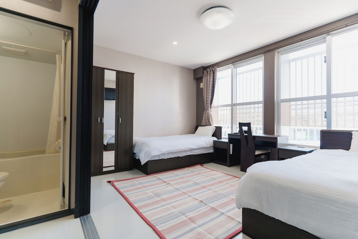 A hotel room with a bed, a desk, a chair, a wardrobe, and a large window.