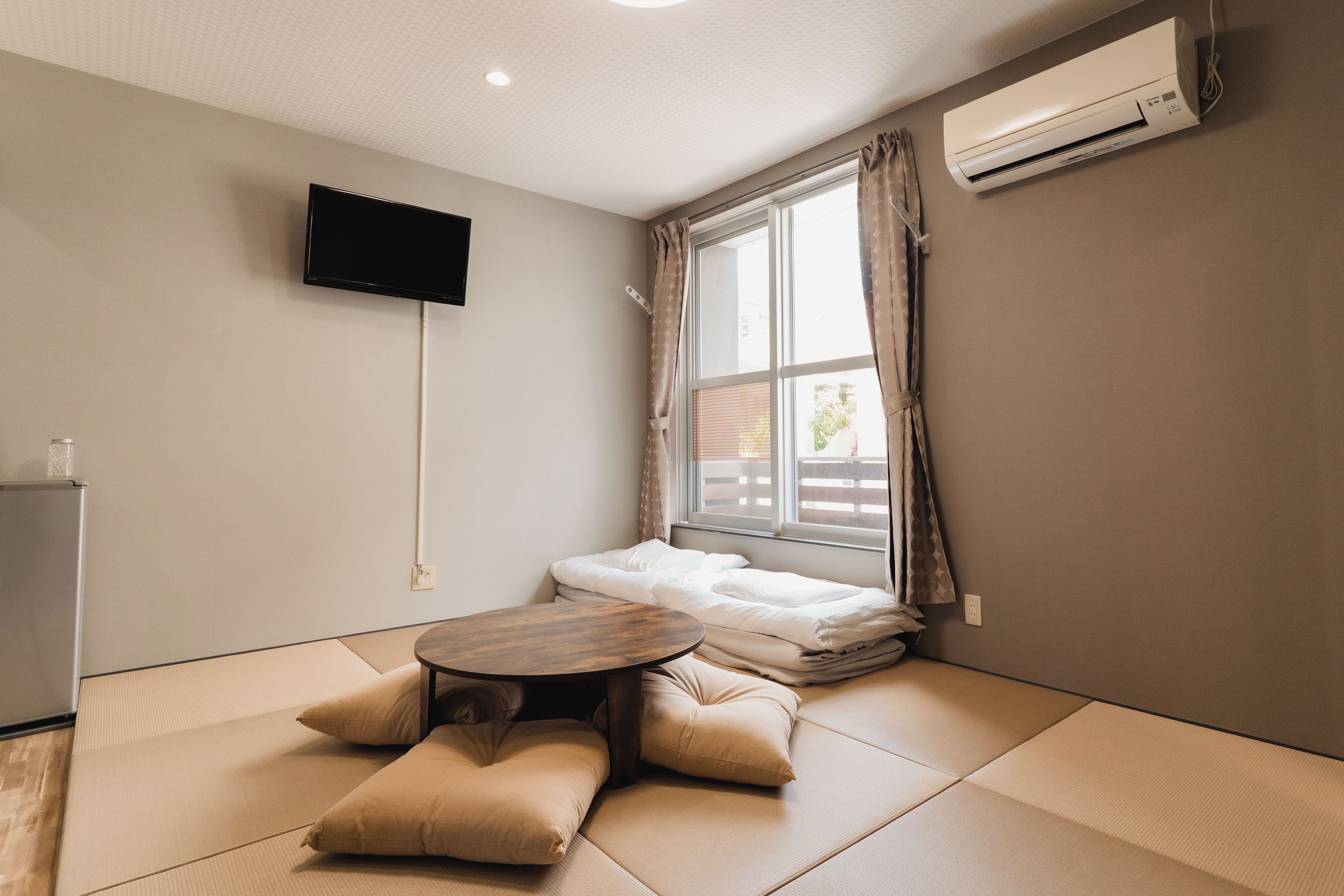 A room with tatami mats, a bed, a TV, and an air conditioner.