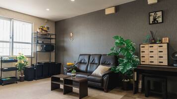 A modern living room with a leather sofa, a coffee table, a bookshelf, and a large potted plant.