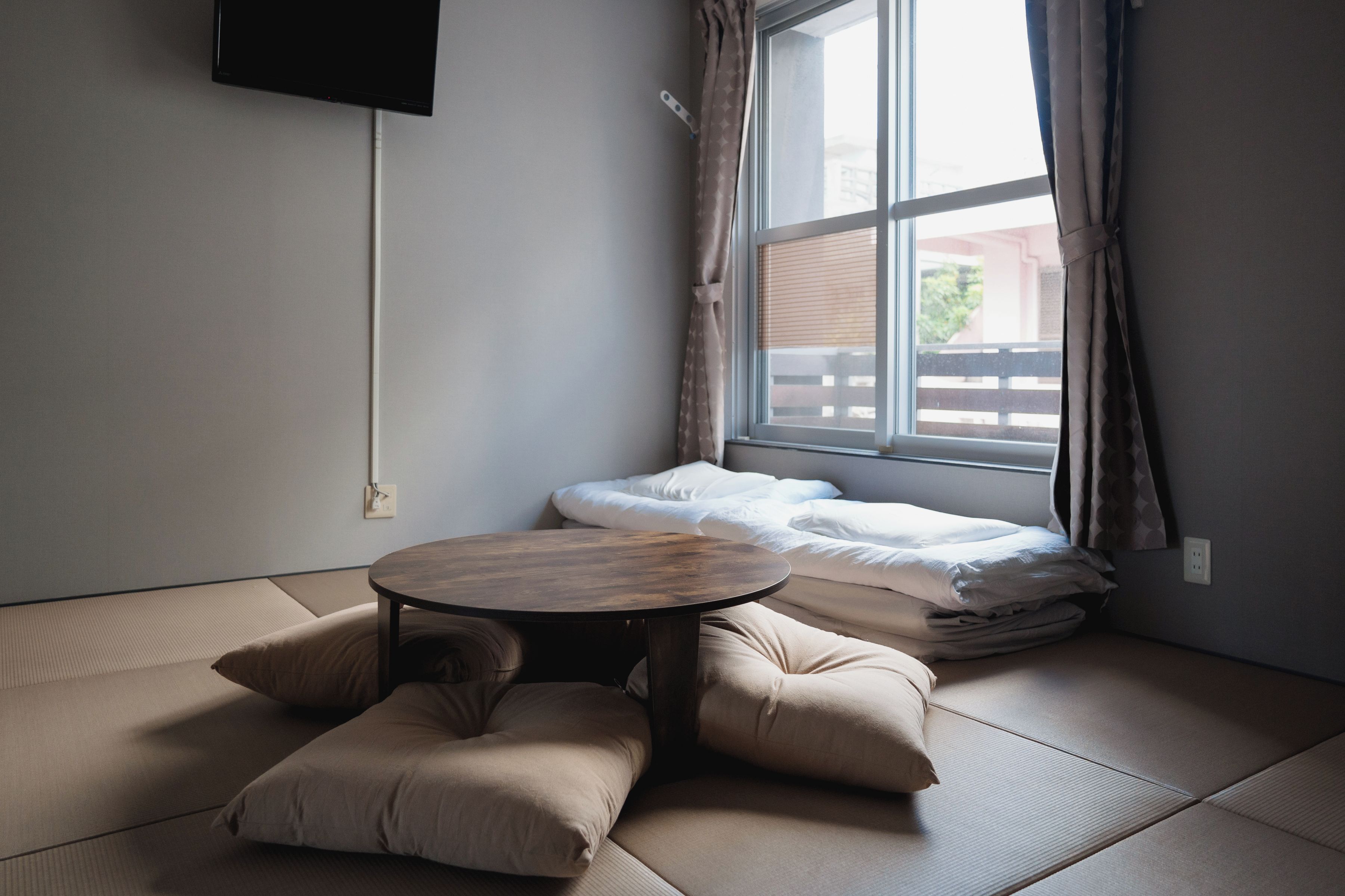 A room with tatami flooring, a low table, and a bed with white bedding.
