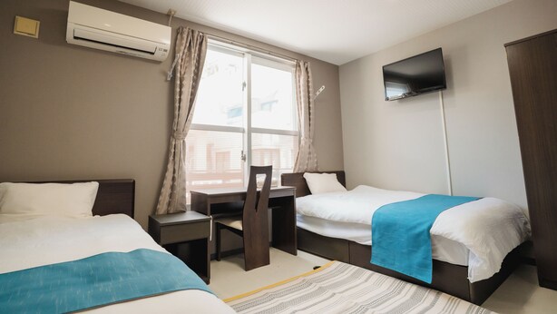 Een hotelkamer met twee bedden, een bureau, een stoel, een aan de muur bevestigde televisie en een airconditioner.