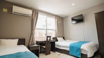 A hotel room with two beds, a desk, a chair, a television, and a window with curtains.