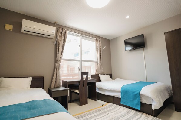 A hotel room with two beds, a desk, a chair, a TV mounted on the wall, and an air conditioning unit on the wall. - ishigaki bus terminal inn (Ishigaki)