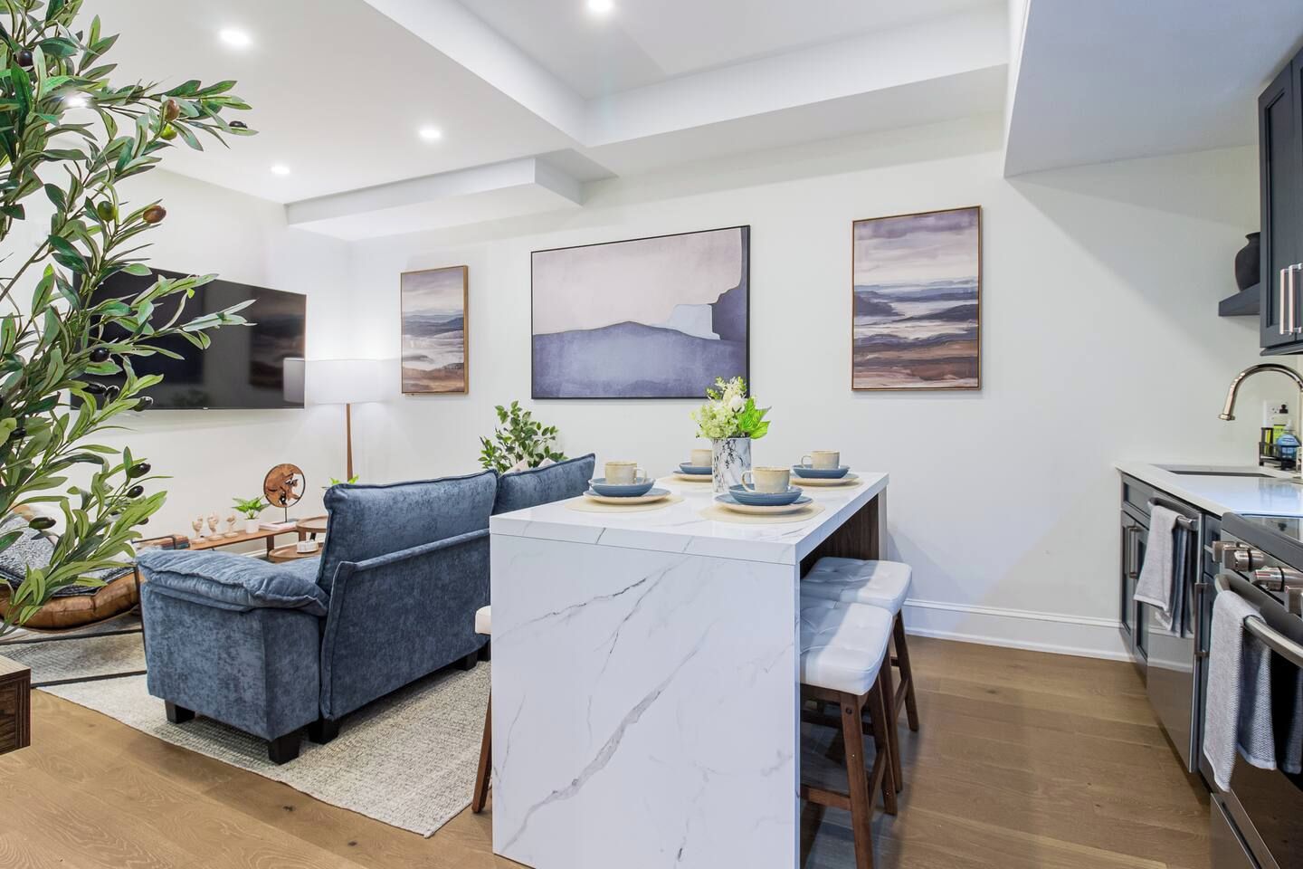 A modern kitchen with a marble island, a dining area with blue sofas, and artwork on the walls.