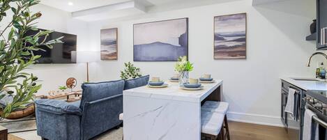 A modern kitchen with a marble island, a dining area with blue sofas, and artwork on the walls.