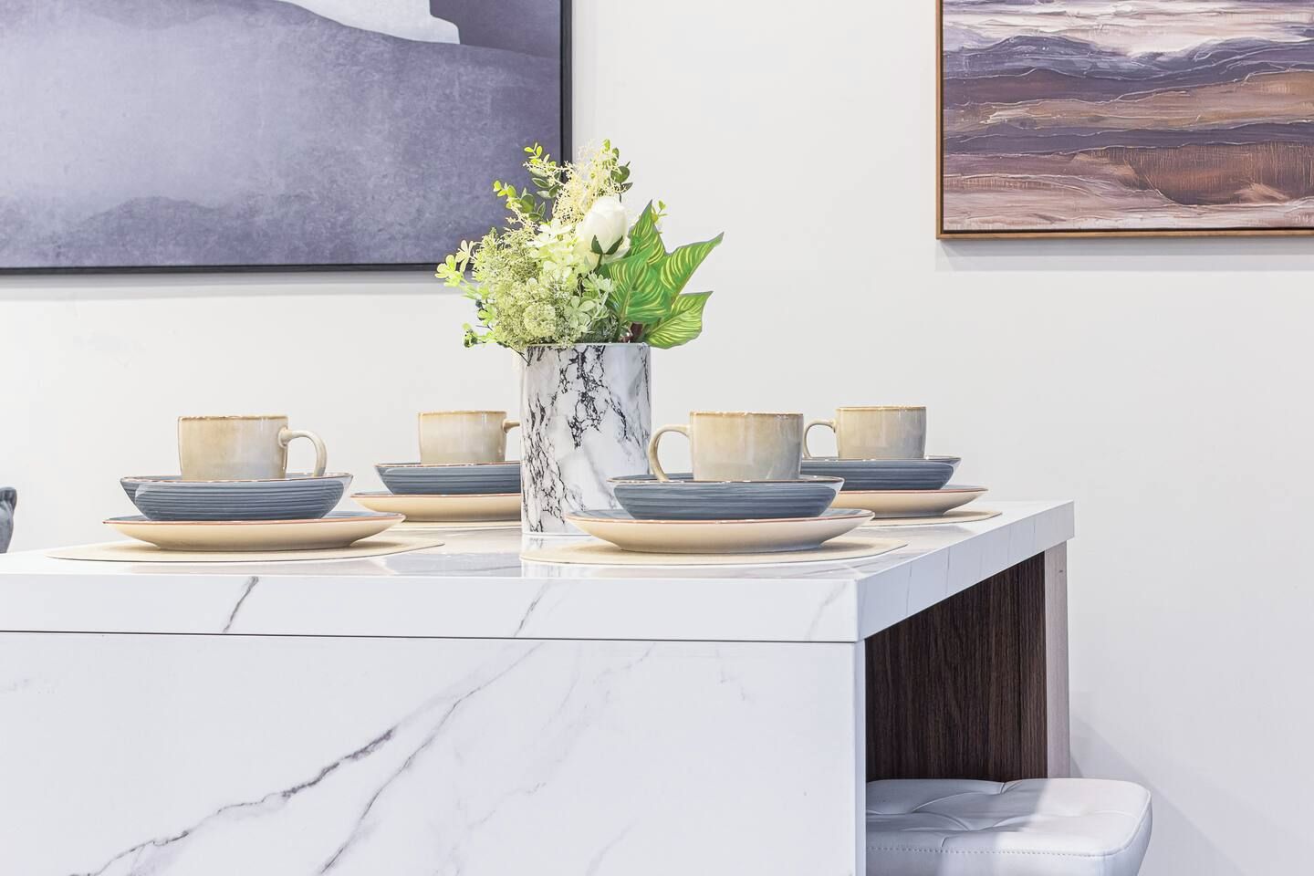 Un coin repas avec une table en marbre, un vase rempli de fleurs et un tableau accroché au mur.