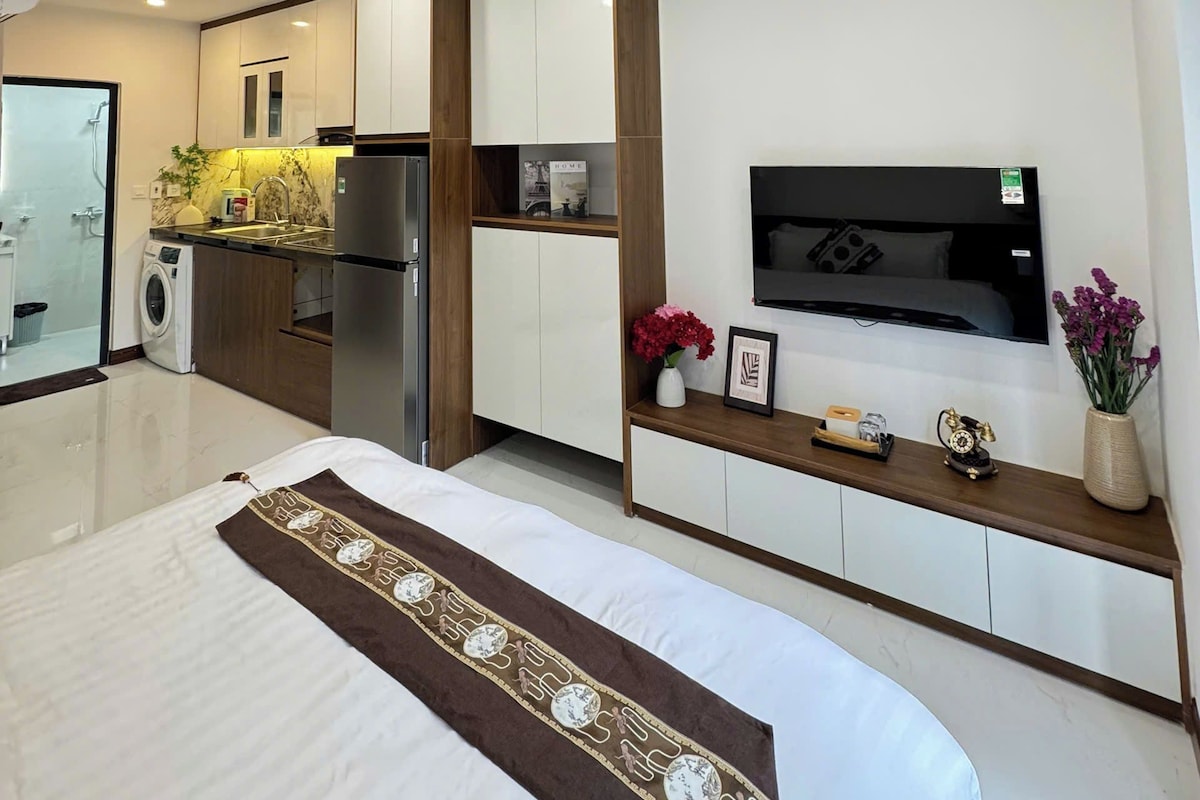Un dormitorio moderno con una cama, un televisor montado en la pared y una pequeña cocina.