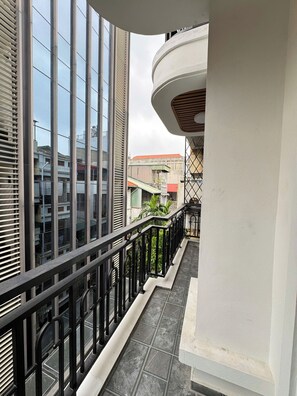Varanda com guarda-corpo de metal preto, vista de edifícios vizinhos e piso de azulejos.