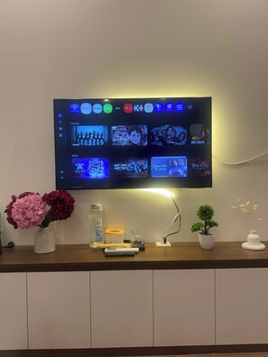 Televisão de tela plana fixada na parede, exibindo diversos serviços de streaming e conteúdo.