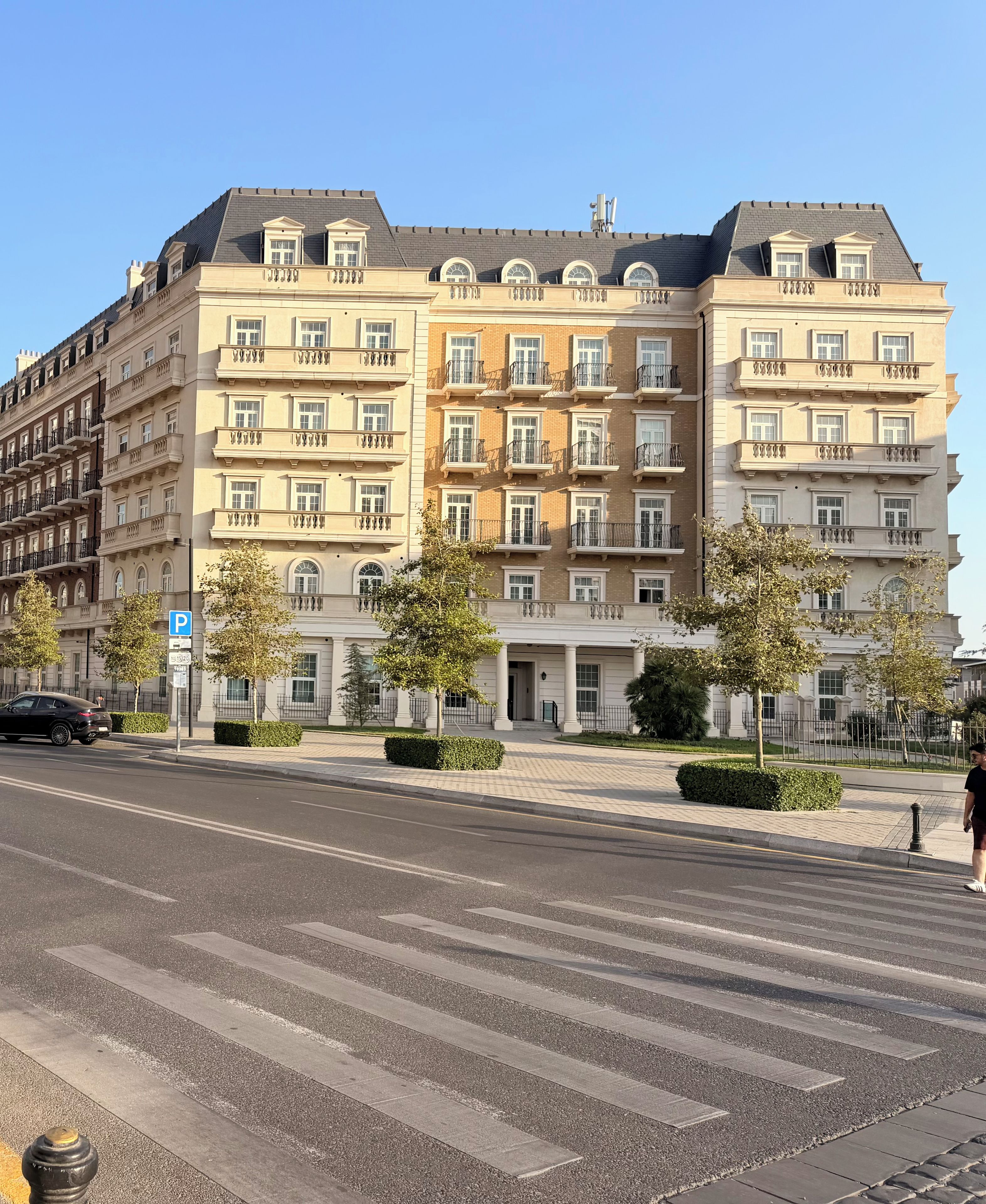 A multi-story hotel with balconies, a parking sign, and a pedestrian crossing.