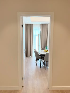 Corredor que leva a uma sala de jantar com uma mesa posta para quatro pessoas, uma garrafa de água e frutas sobre a mesa.