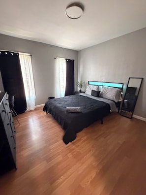 Ein Schlafzimmer mit einem Bett, einem Schminktisch, einem Spiegel und einem Fenster mit Vorhängen.
