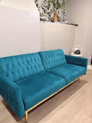 Ein dunkelblaues, gepolstertes Sofa mit Holzbeinen, stehend auf einem Holzboden.