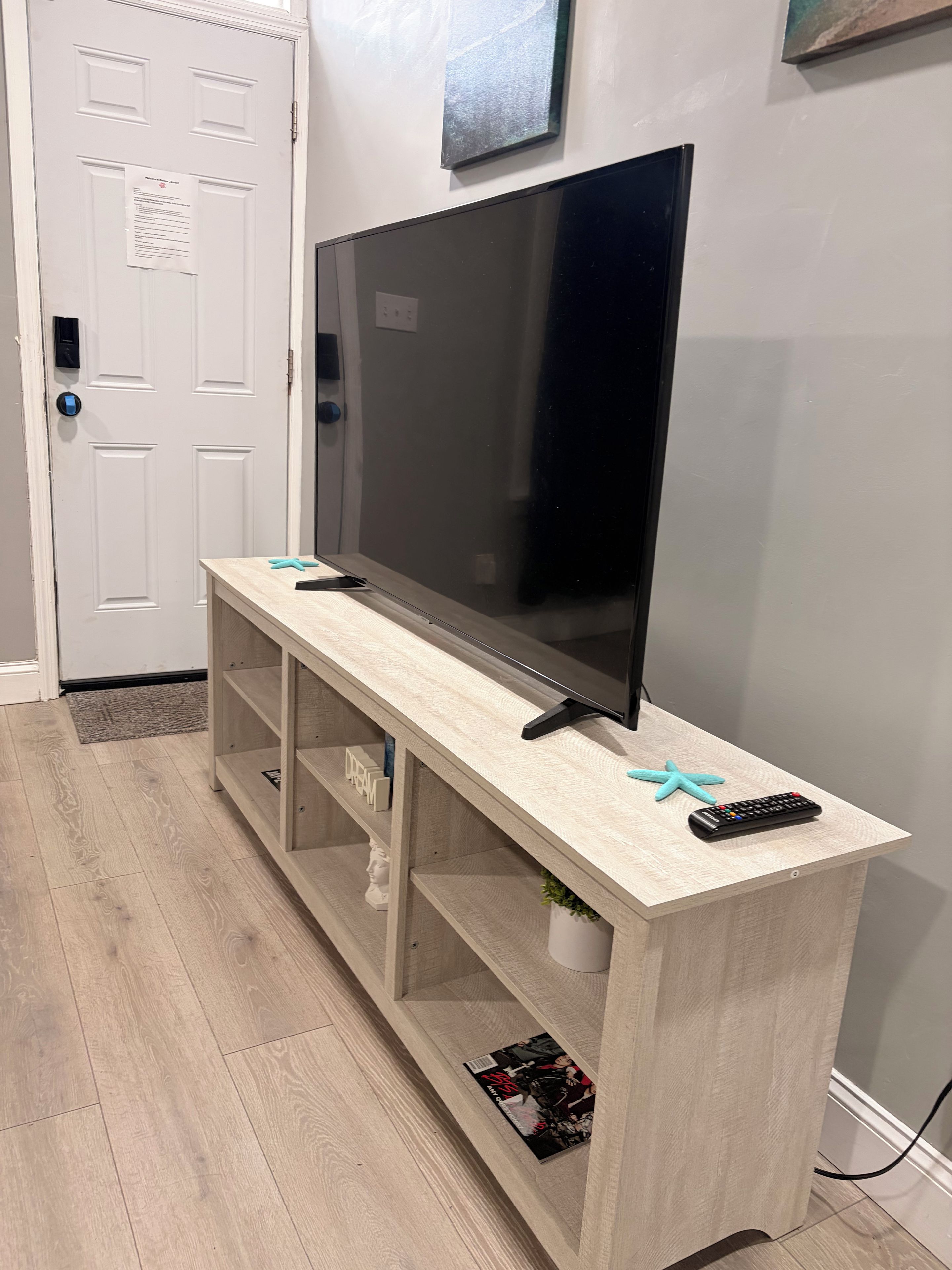 A flat-screen TV on a wooden TV stand with a remote and a starfish decoration.
